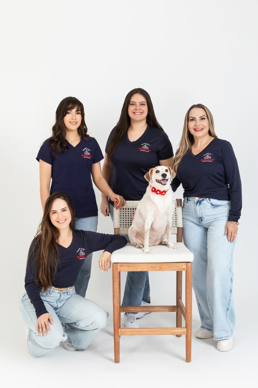 The Super Pet team four certified groomers in navy uniforms posing with a happy dog wearing a red collar